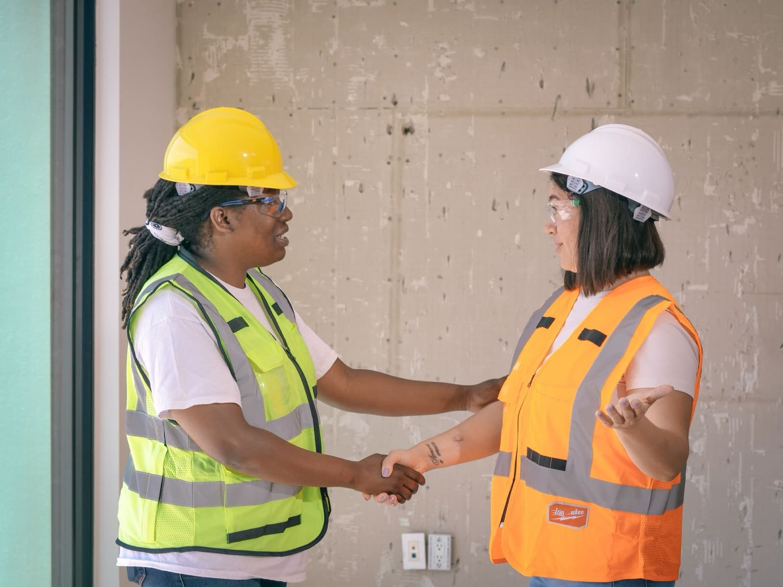 Two workers in safety vests shaking hands on a job site