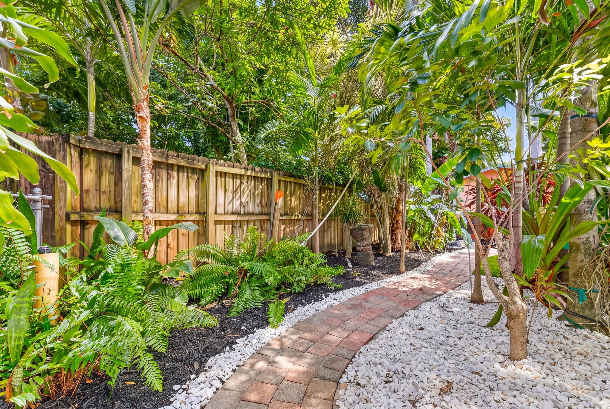 Paver walkway with white rock beds along the side fence