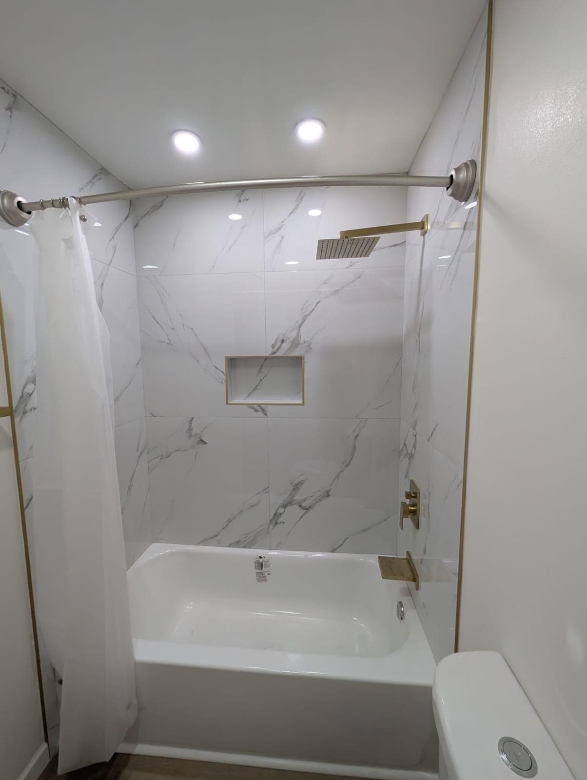 Tub surround in marble-look tile with gold trim and niche