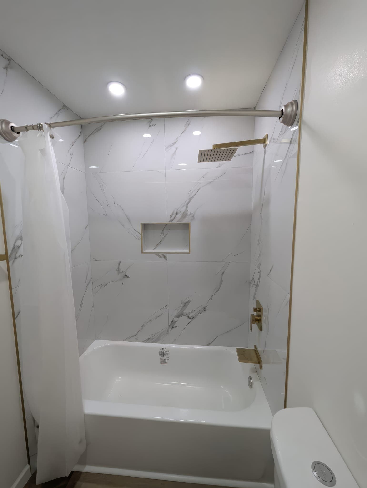 Tub surround in marble-look tile with gold trim and niche