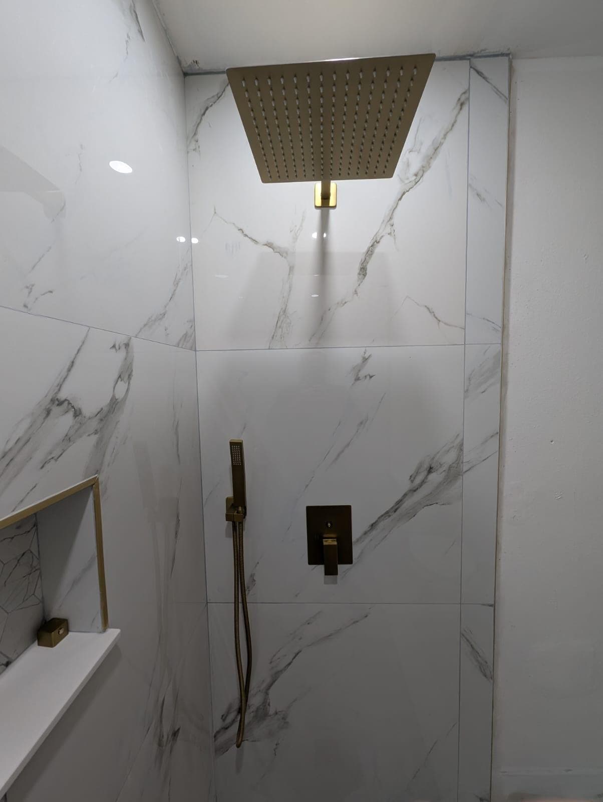 Brushed gold shower valve and hand shower on marble-look tile
