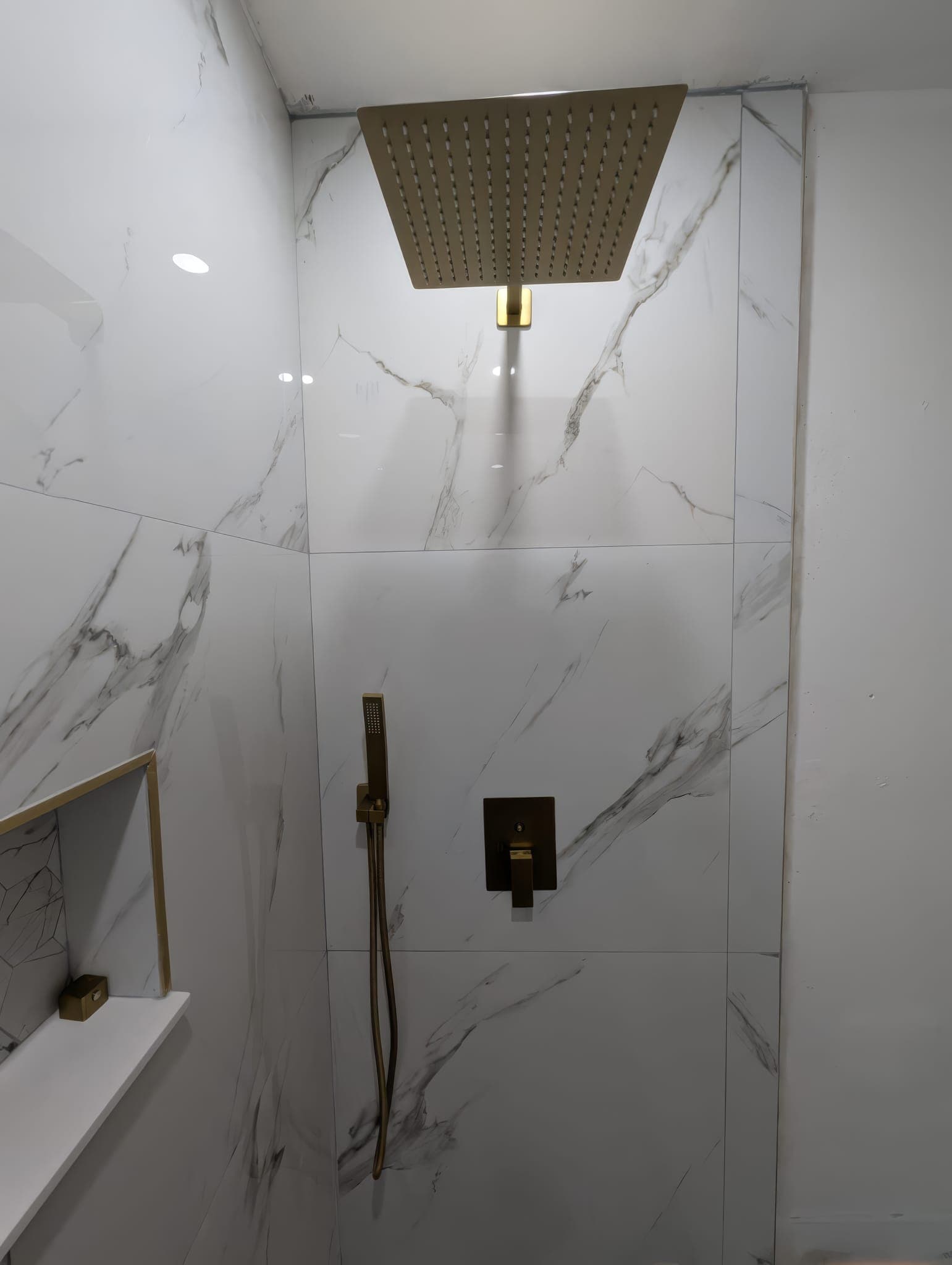 Brushed gold shower valve and hand shower on marble-look tile