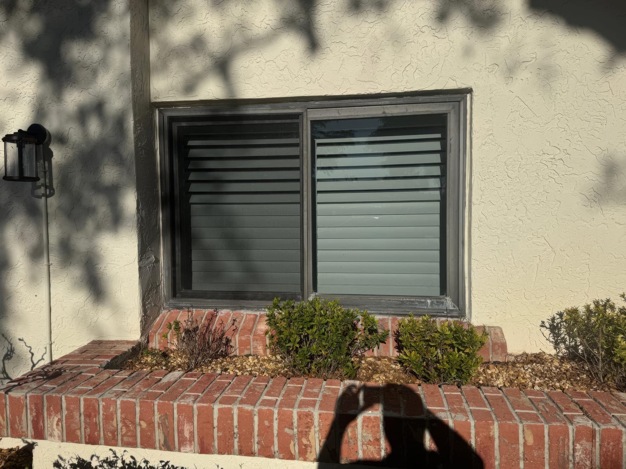 Original aluminum window with a roll-down hurricane shutter above a brick planter, before