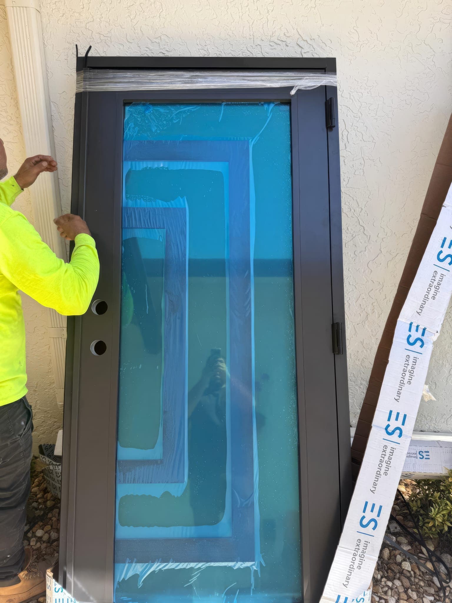 Crew carrying a new bronze-framed impact door with protective film into position