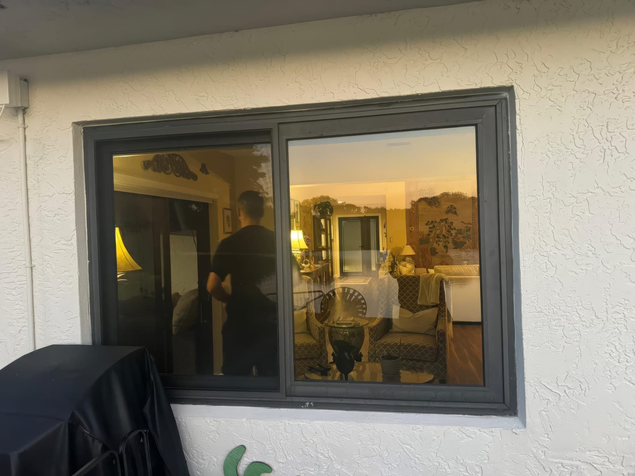 Horizontal slider impact window on the side of the house, lit from inside at dusk