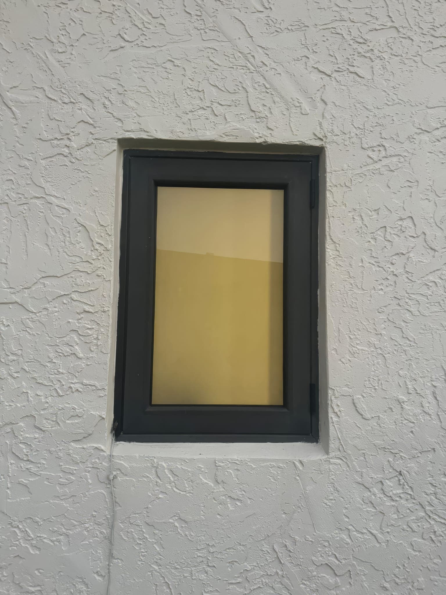Small bronze-framed impact window set into the textured stucco wall