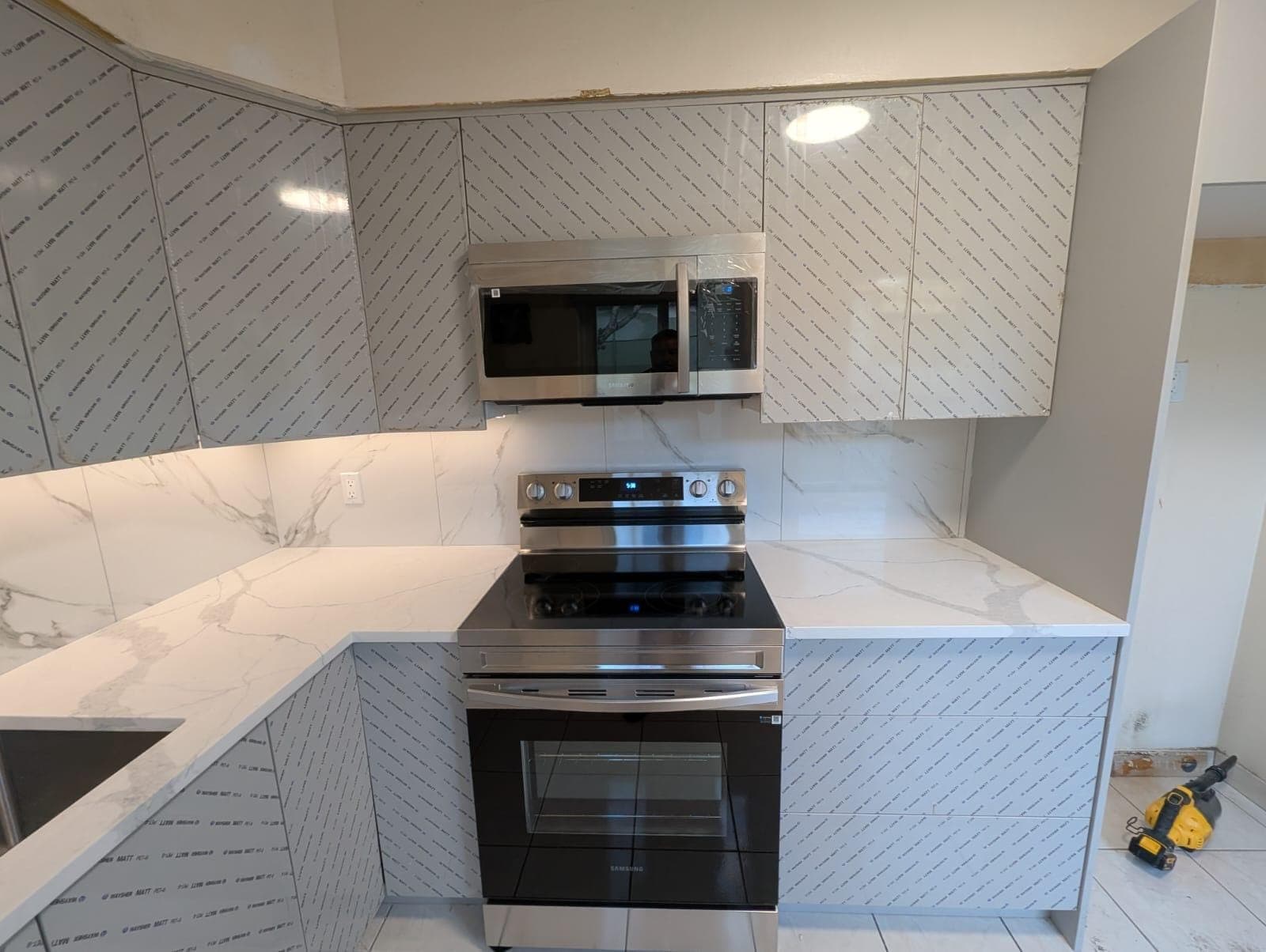 Grey high-gloss kitchen cabinets being installed with marble-look backsplash