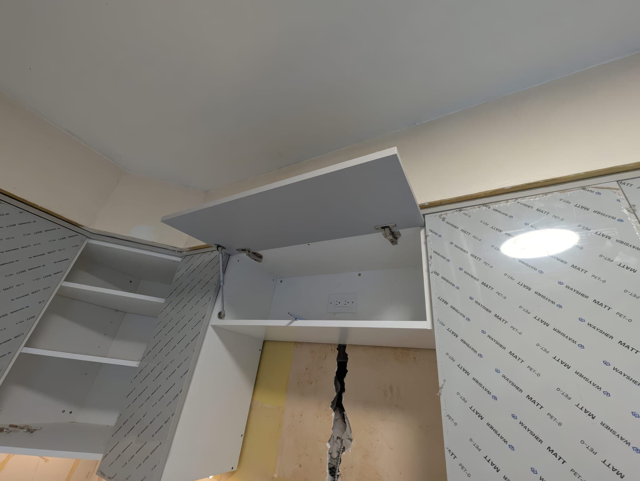 Upper cabinets being hung with protective film still on