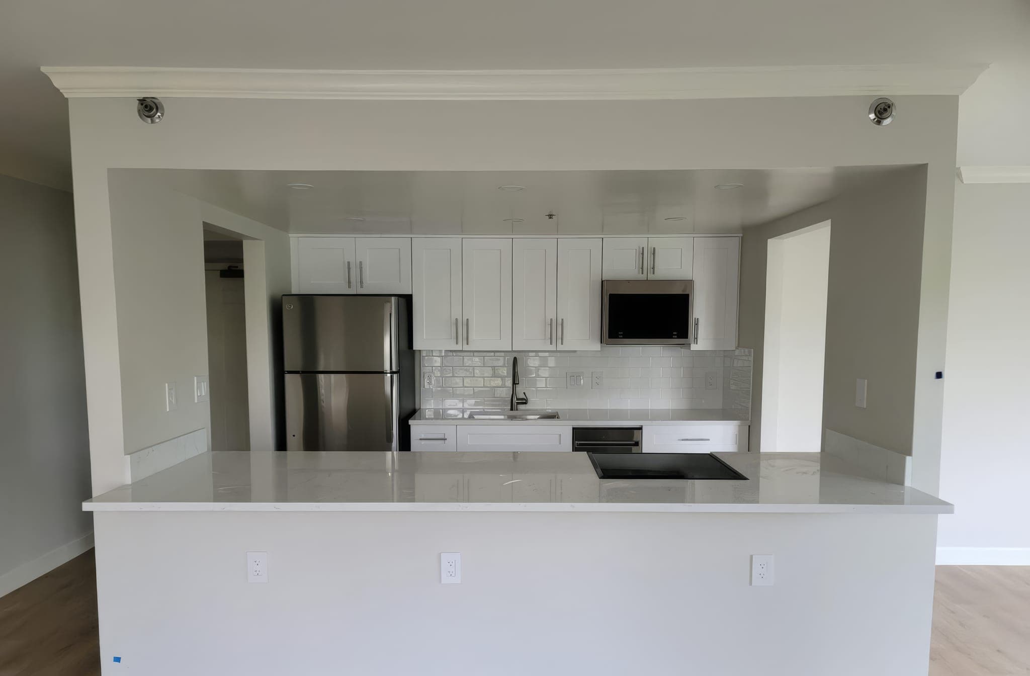 Remodeled kitchen with white shaker cabinets, quartz peninsula and stainless refrigerator