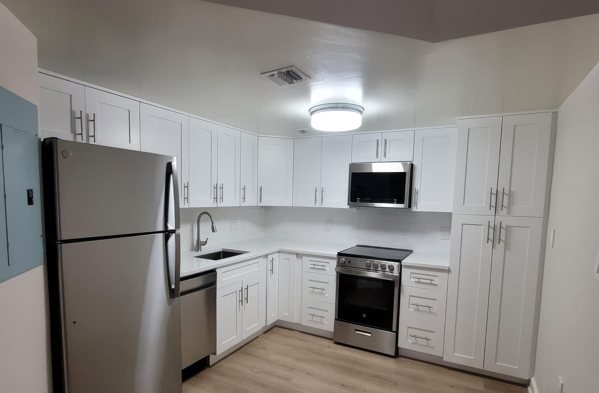 L-shaped white kitchen with new flooring and flush ceiling light