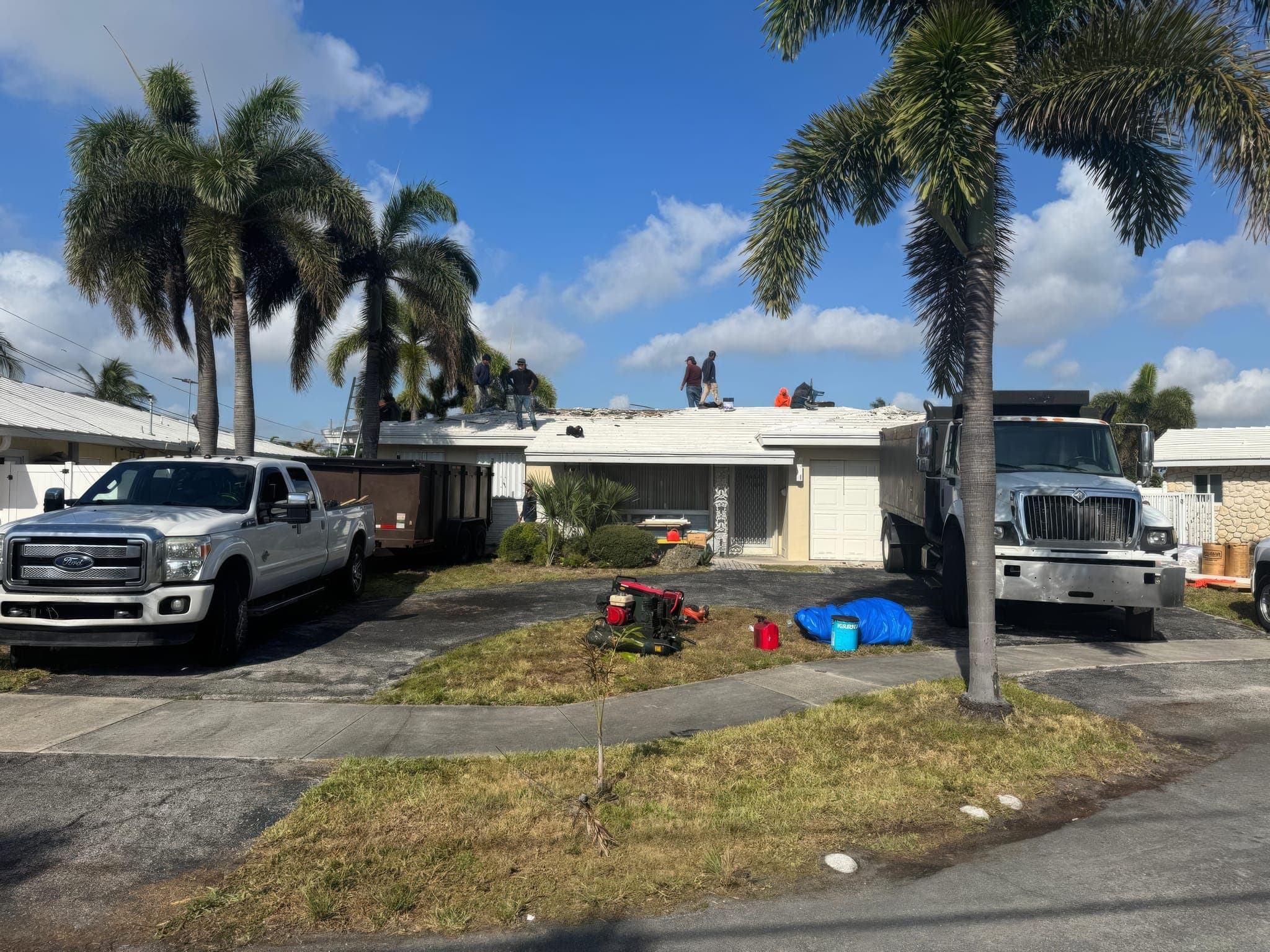 Crew on the roof during tear-off, dump trailer and trucks in the driveway