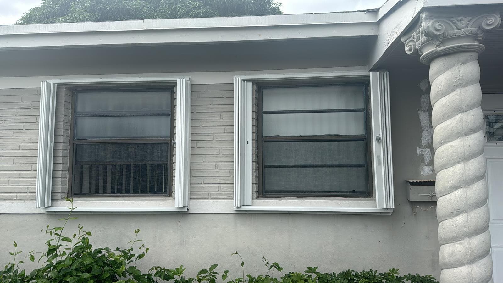 Two original single-pane windows on a stucco wall before replacement