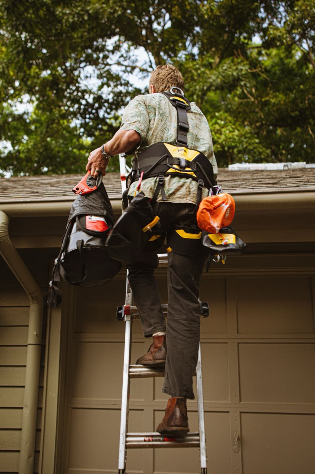 Roofer in safety gear climbing a ladder to repair a residential roof