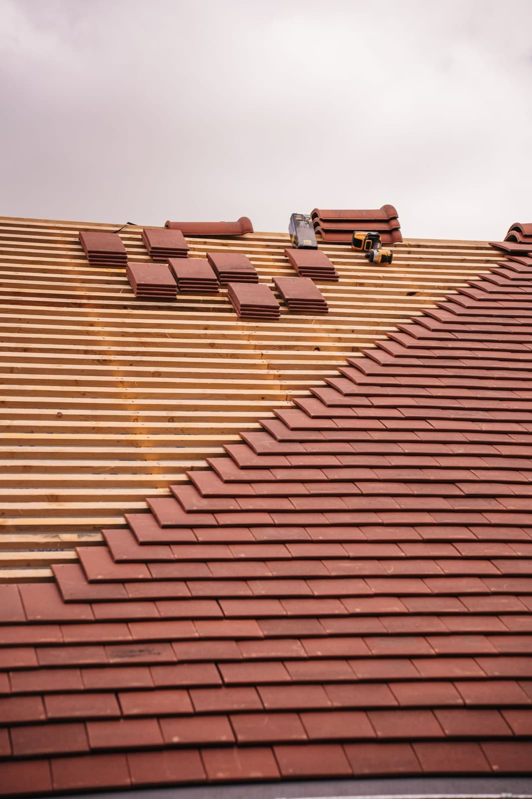Clay roof tiles being installed over new battens on a sloped roof